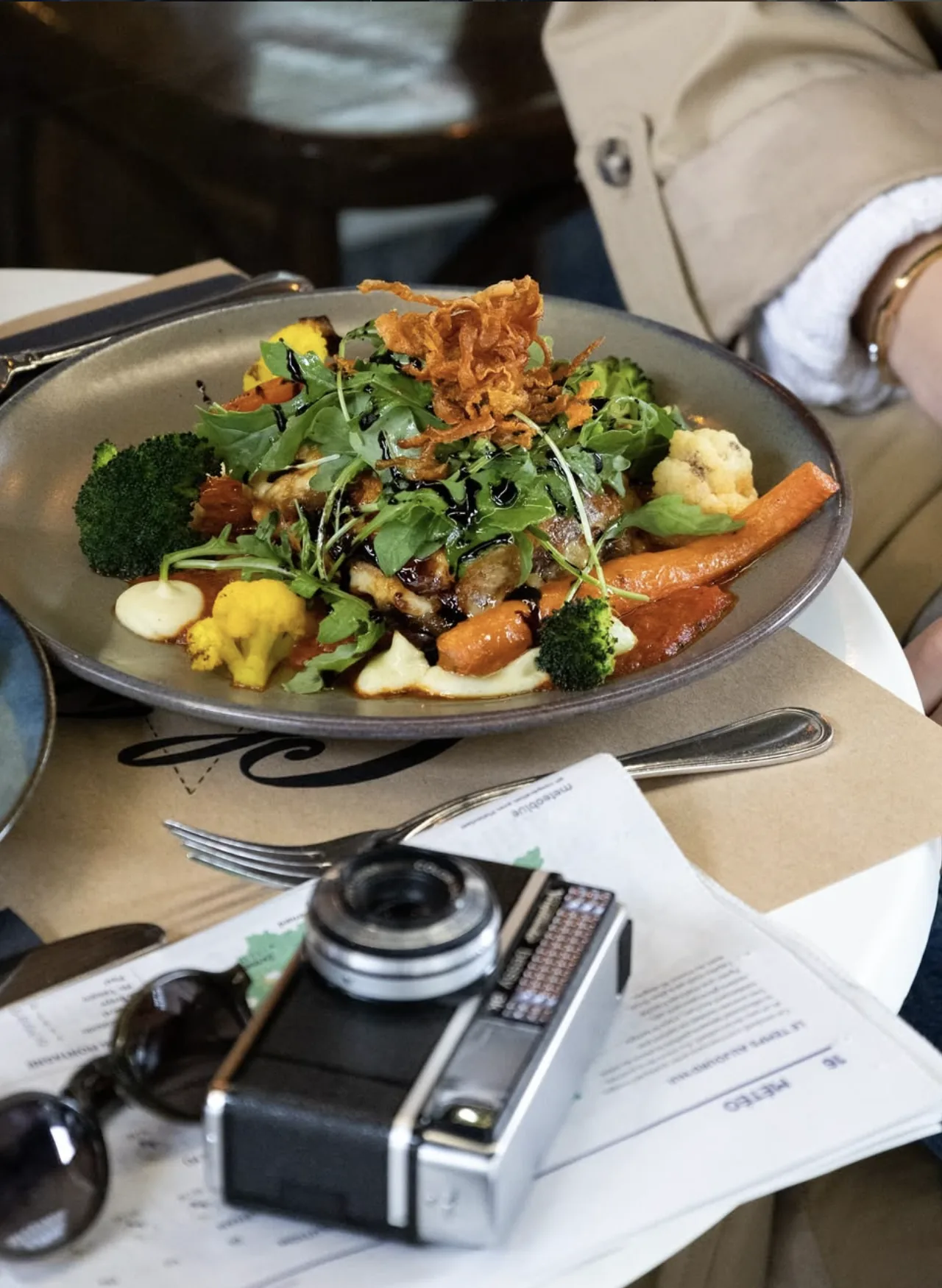 Une assiette de poisson et de légumes rôtis, roquette et oignons frits, posée sur une table de la salle.